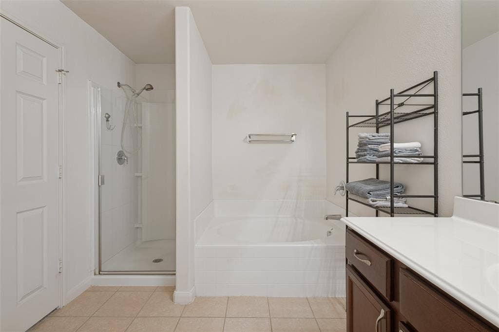 Bathroom featuring a deep-basin soaking tub with tile surround, separate glass-enclosed shower, wood-finish vanity cabinet, and tile flooring