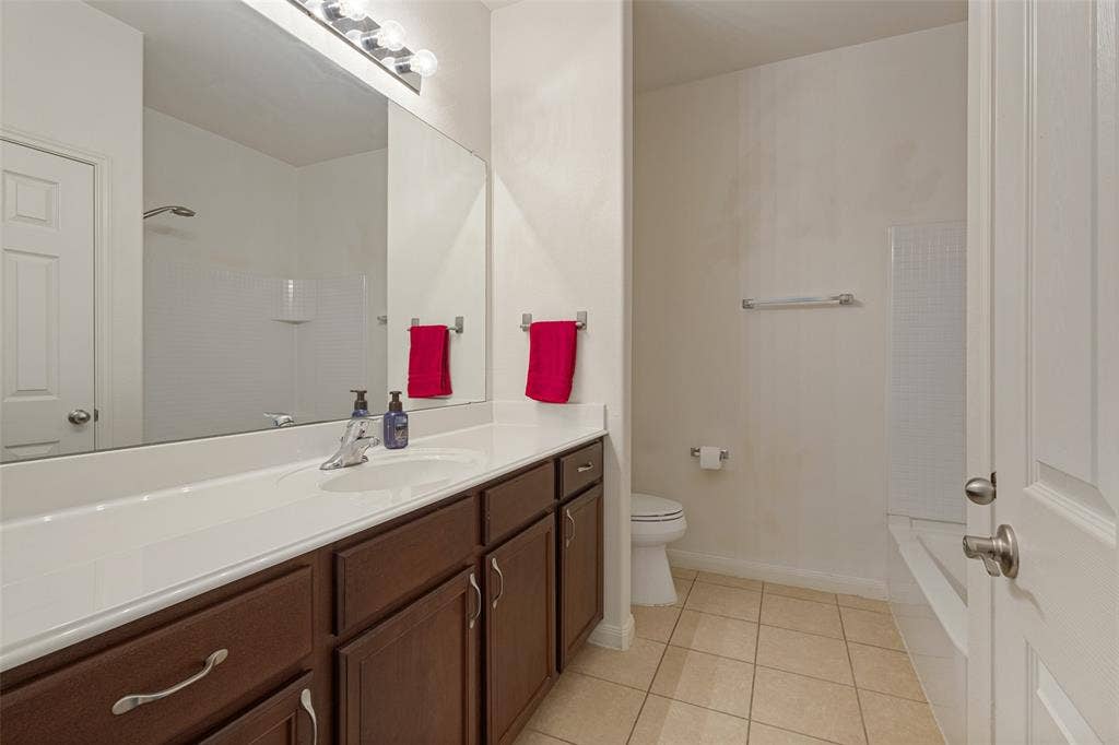 Bathroom featuring a dark wood-finish vanity with a white integrated countertop, large wall-mounted mirror, ceramic tile flooring, and a shower-tub combination with tile surround