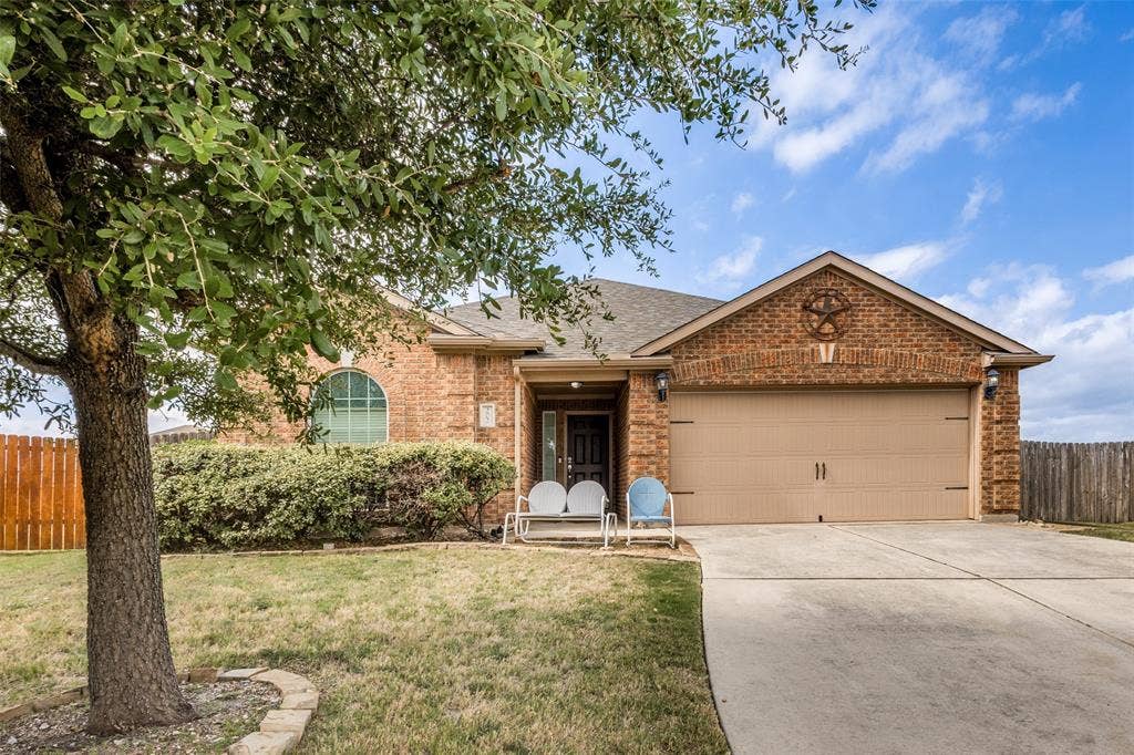 Brick exterior facade featuring a front-facing gable, arched window, concrete driveway, and established mature tree