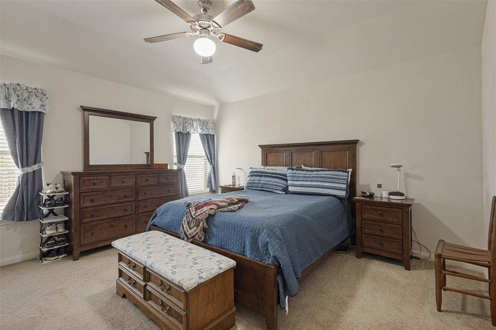 Vaulted ceiling, ceiling fan with light fixture, wall-to-wall carpeting, and dual windows