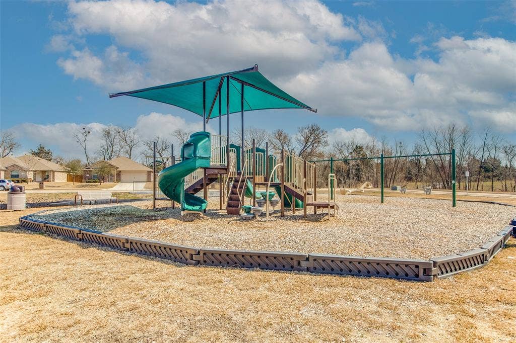 Playground structure featuring a shaded canopy, a spiral slide, and integrated stairs, set within a gravel-surfaced area with a decorative border