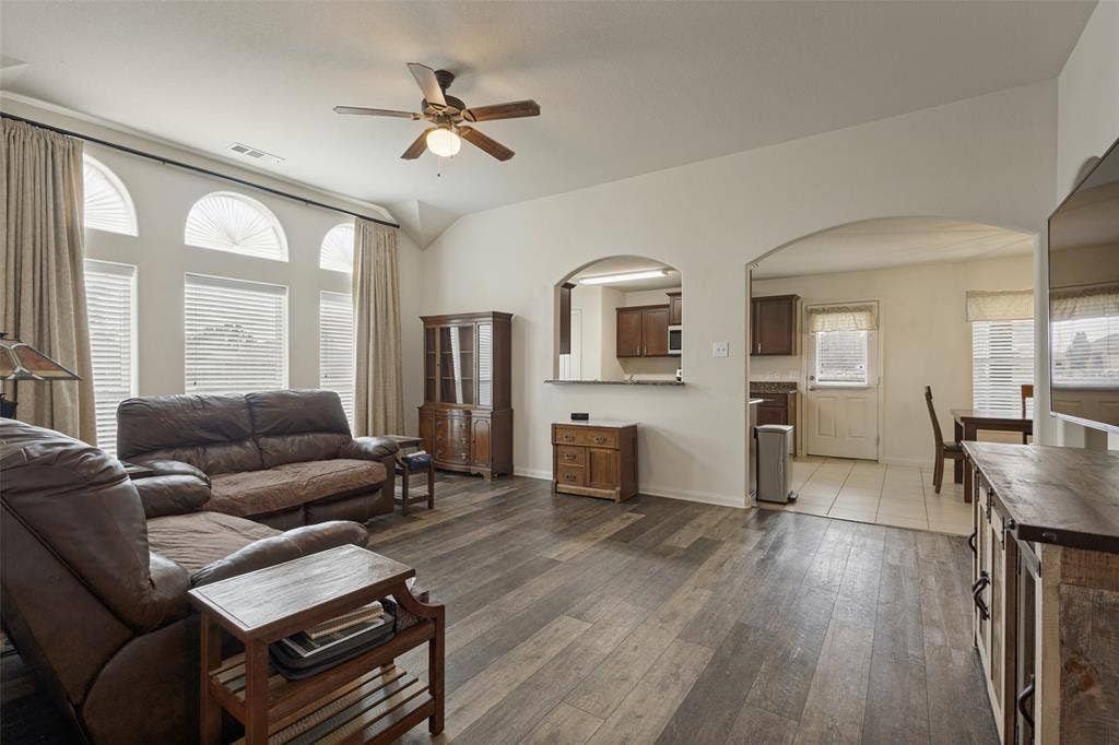 Living area featuring vaulted ceilings, wood-finish flooring, a ceiling fan, and arched wall openings