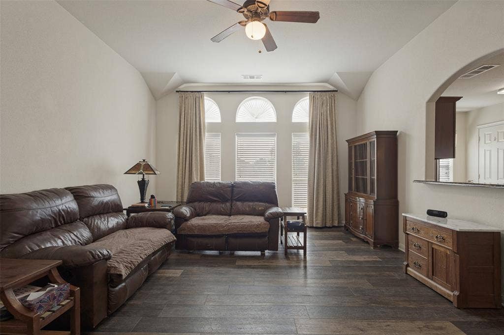 Vaulted ceiling living area featuring wood-finish plank flooring, trio of arched windows, and a central ceiling fan