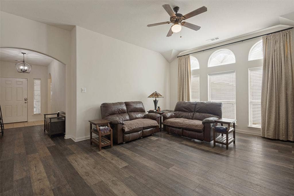 Living area featuring wood-finish flooring, vaulted ceilings, arched windows, and a ceiling fan with integrated lighting