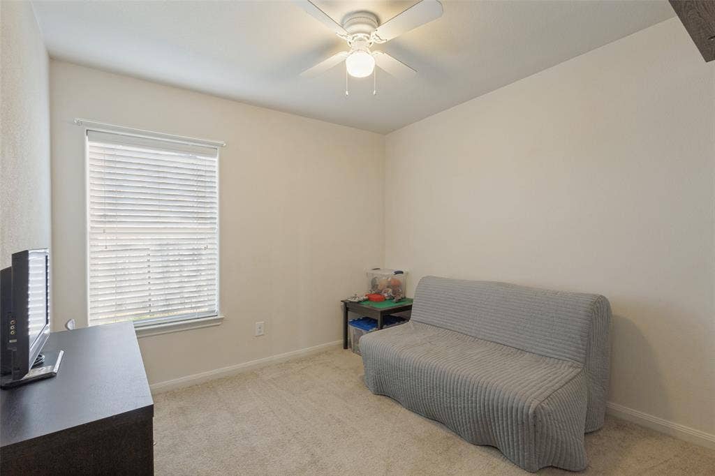 Neutral-toned carpeted flooring, wall-mounted window blinds, and a white ceiling fan with integrated lighting