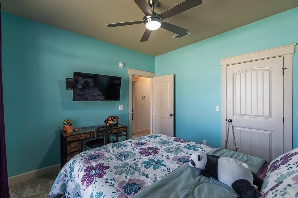 Neutral-toned carpet, ceiling fan with integrated lighting, multi-panel doors with substantial trim, and wall-mounted television bracket