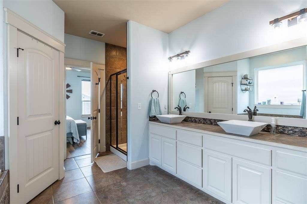 Bathroom featuring a dual-sink vanity with white cabinetry, square vessel sinks, a large framed mirror, and a walk-in shower with tile surround
