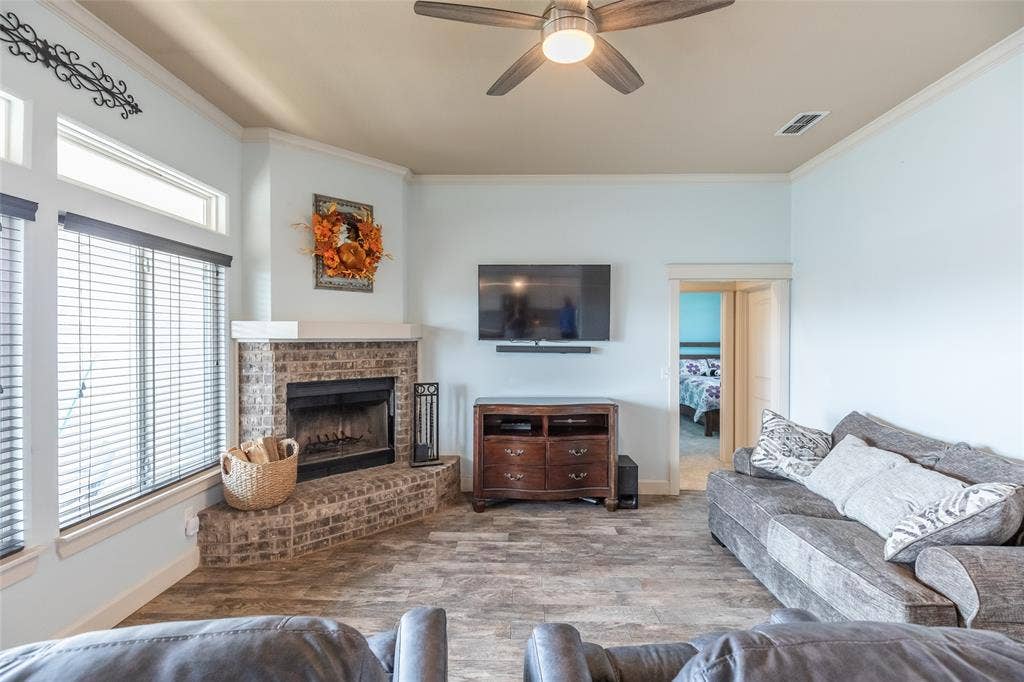 Corner fireplace featuring brick masonry construction, multi-pane windows with horizontal blinds, ceiling fan, and tile flooring