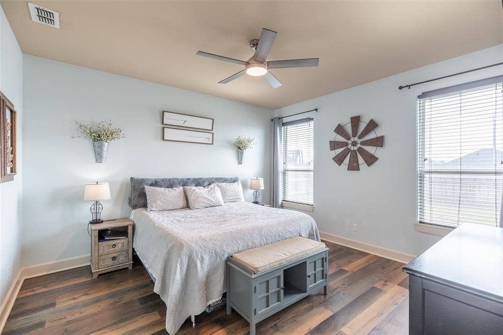 Room featuring wood-finish flooring, a multi-blade ceiling fan with integrated lighting, and dual windows equipped with horizontal blinds
