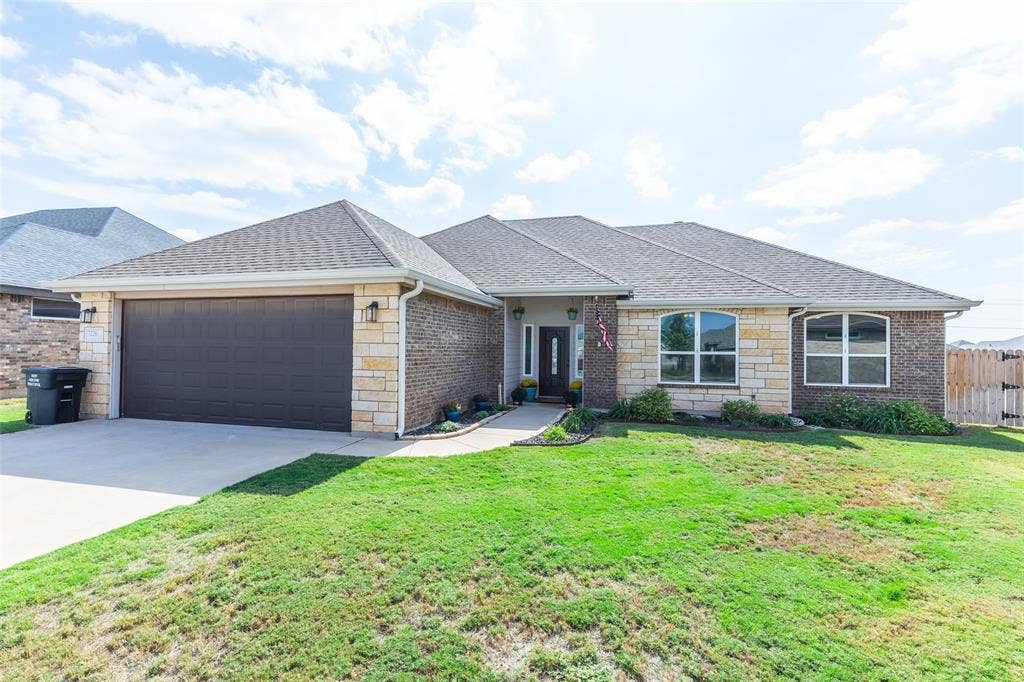 Exterior facade featuring a combination of brick and stone masonry, hip roof construction, two-car garage, arched window accents, and a concrete driveway