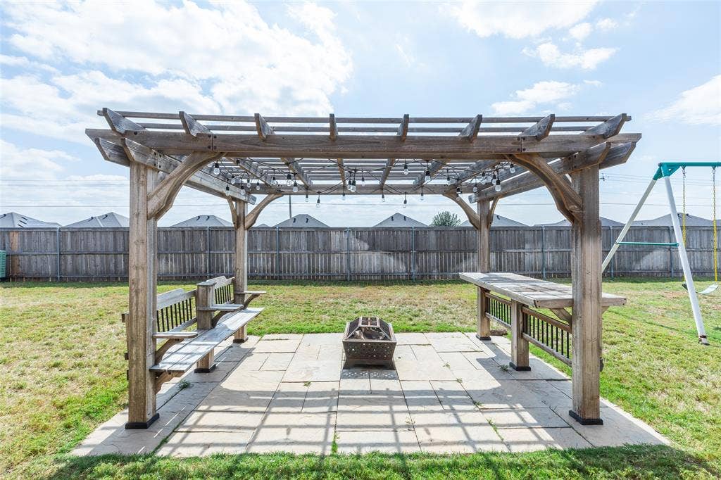 Backyard area featuring a wooden pergola with integrated string lighting, a concrete paver patio, and built-in wooden benches