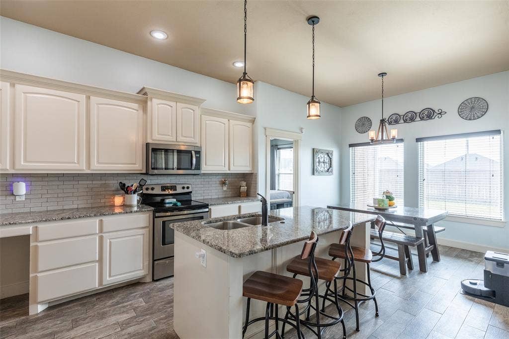 Kitchen featuring white cabinetry, stone-finish countertops, stainless steel appliances, a central island with an integrated sink, and wood-finish tile flooring