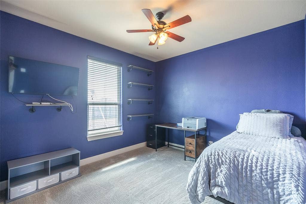 Bedroom featuring neutral carpeting, a central ceiling fan with integrated lighting, a window with horizontal blinds, and four built-in wall-mounted shelves