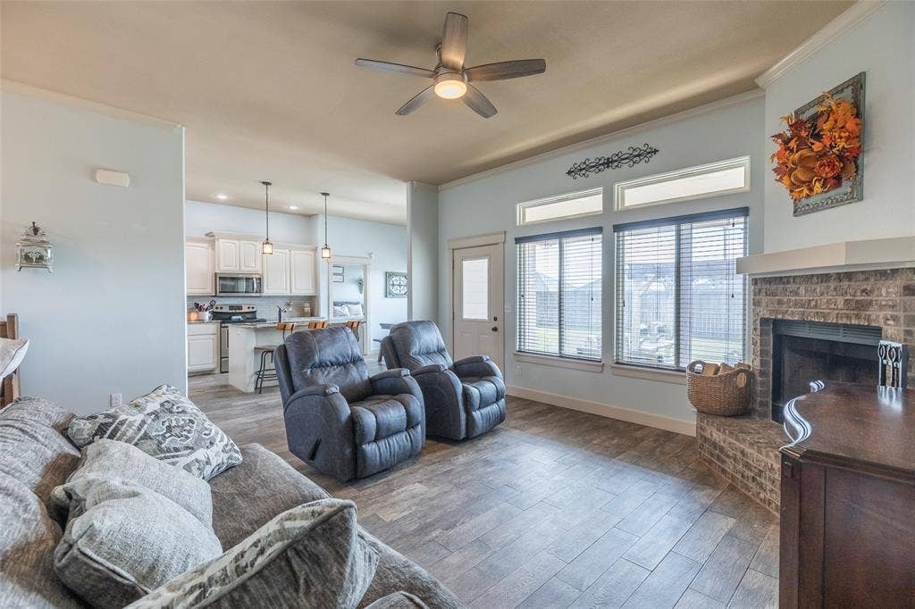 Open-concept interior featuring wood-finish flooring, a brick masonry fireplace, large windows with transoms, and a kitchen equipped with cabinetry and pendant lighting