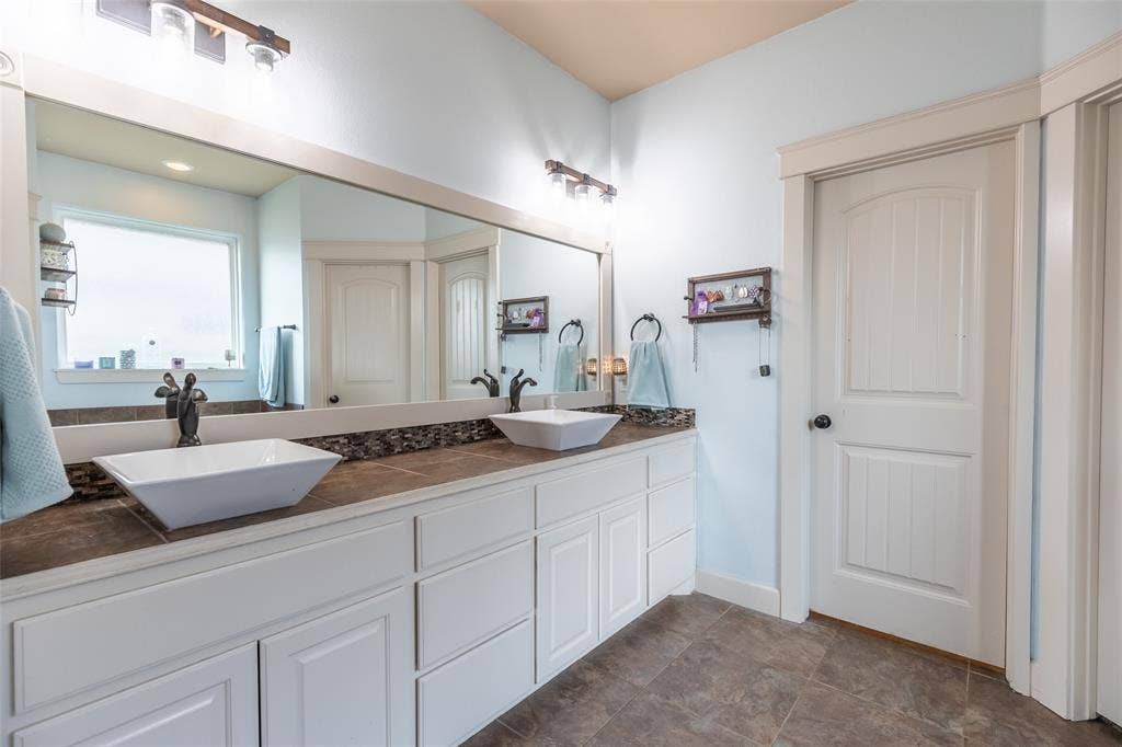 Dual vanity featuring white shaker-style cabinetry, rectangular vessel sinks, stone-finish countertops, and dual wall-mounted light fixtures
