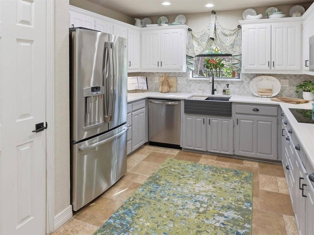 Kitchen featuring stainless steel appliances, white and gray shaker-style cabinetry, a farmhouse-style apron sink, patterned tile backsplash, and stone-finish flooring