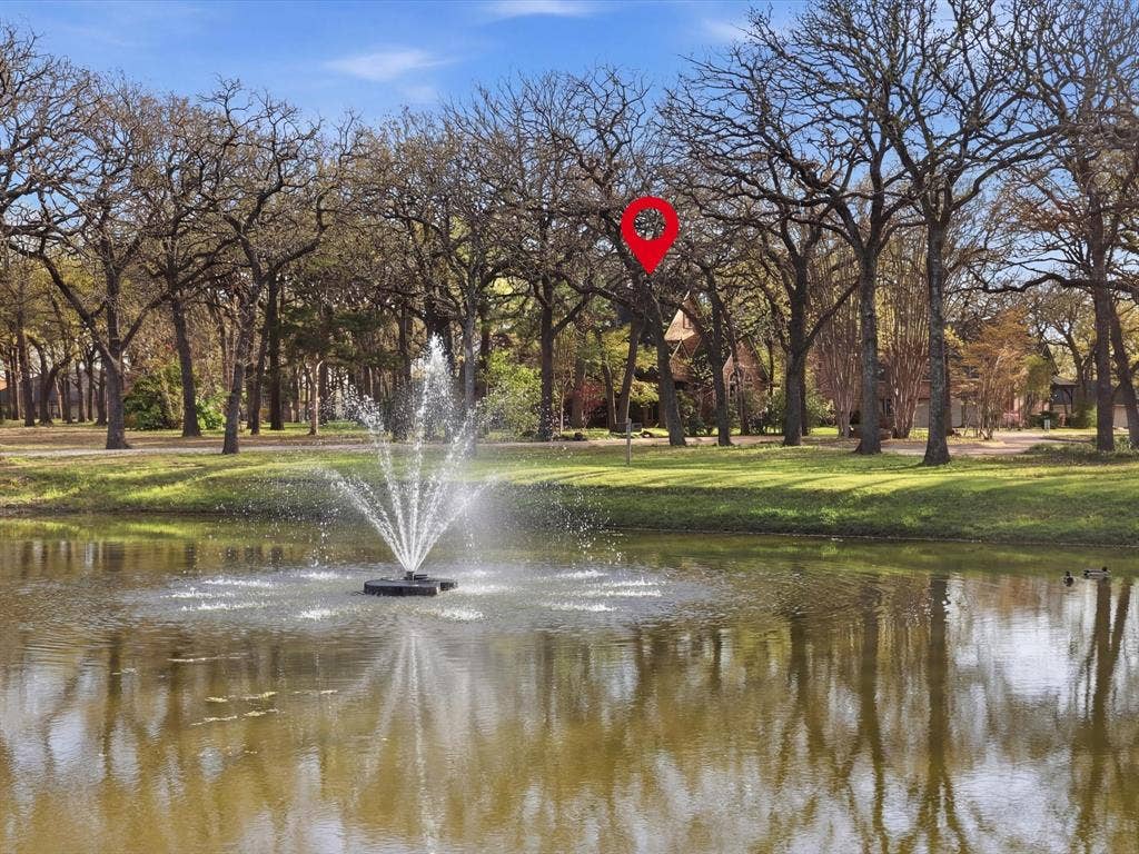 Water feature with centered fountain, sprawling natural landscape, and mature trees situated on a pond-front lot
