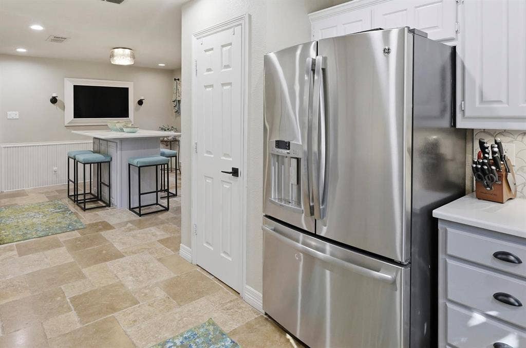 Kitchen featuring stone-tile flooring, stainless steel French-door refrigerator, shaker-style cabinetry, and a central island with countertop seating