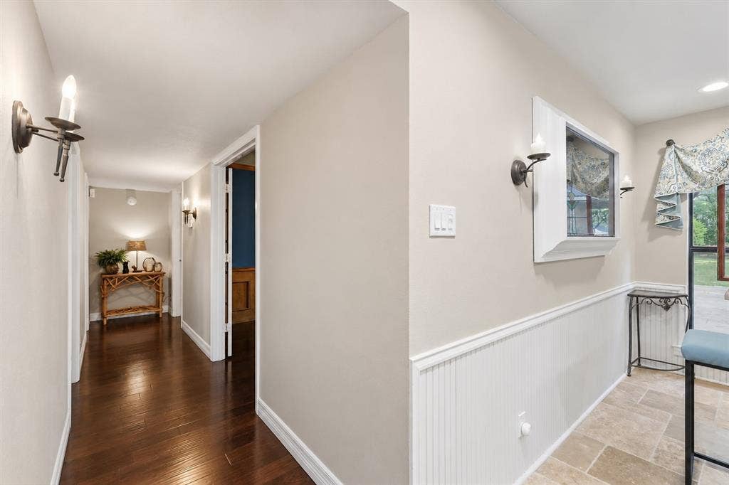 Interior corridor featuring wood-finish flooring, white beadboard wainscoting, and wall-mounted candle-style sconces