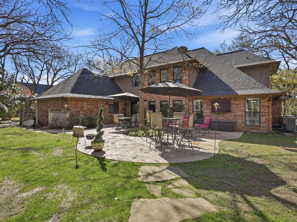 Multi-story brick exterior featuring a stamped concrete patio, irregular stone pathway, and mature tree canopy