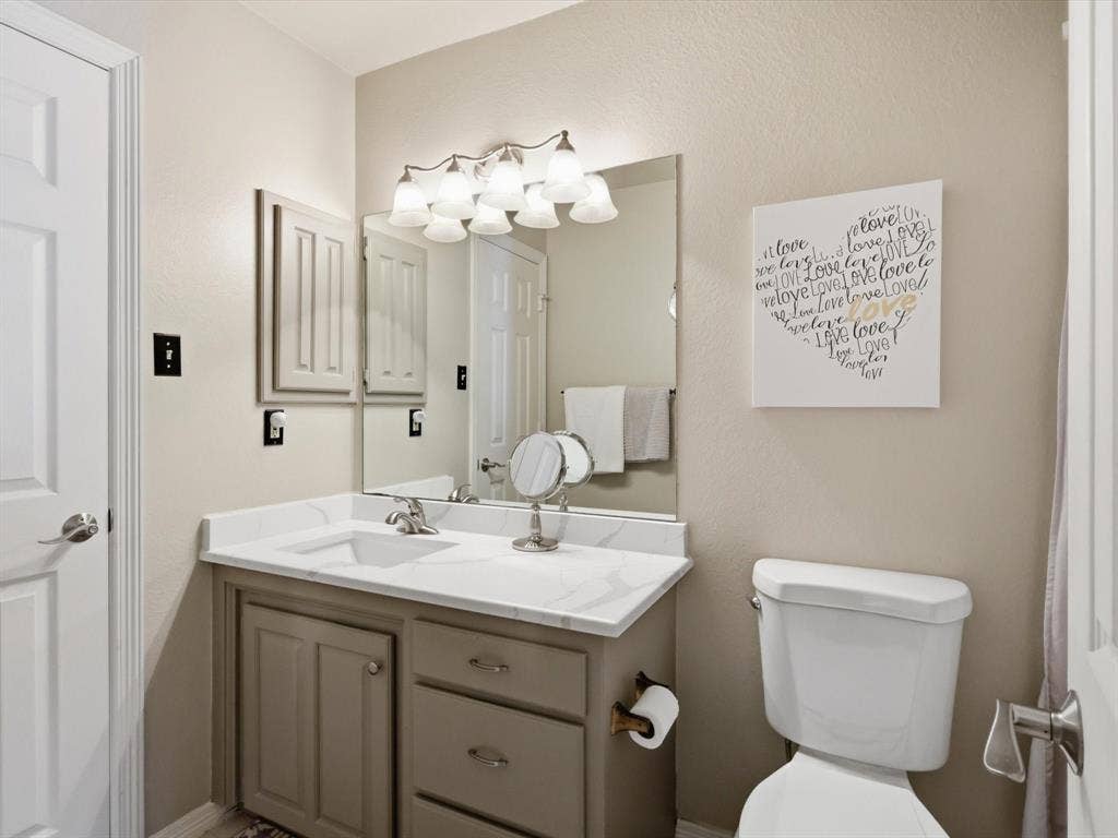 Bathroom vanity featuring a stone-composite countertop with integrated sink, undermount faucet, multi-drawer cabinetry, and a wall-mounted light fixture above a framed mirror