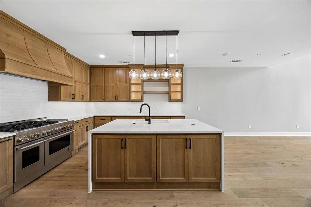 Kitchen featuring wood-finish cabinetry, a large central island with a white surface, professional-grade range, custom wood range hood, and linear pendant lighting