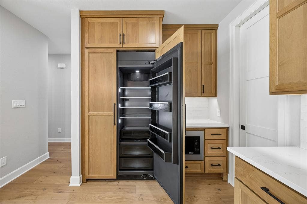 Custom wood cabinetry featuring an integrated refrigerator, white stone-finish countertops, built-in microwave, and light-toned wood-finish flooring