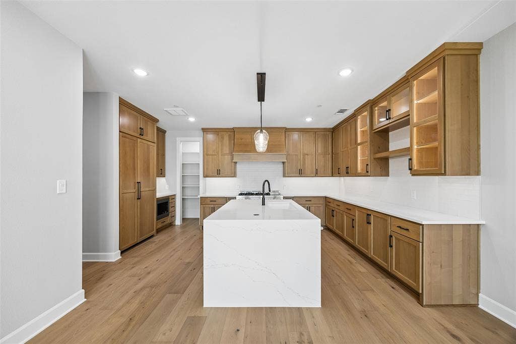 Kitchen featuring shaker-style cabinetry with integrated panel-ready appliances, a central quartz-topped island, wood-finish flooring, recessed lighting, and a walk-in pantry