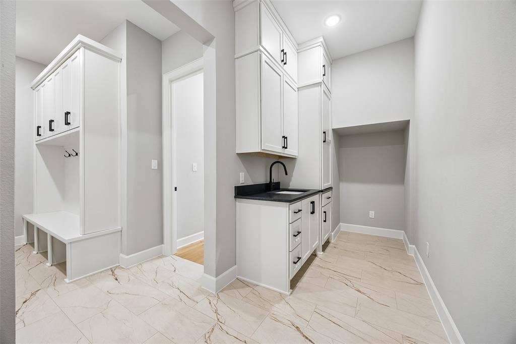 Custom mudroom featuring built-in cabinetry with bench seating, white shaker-style cabinetry, matte black hardware, dark stone countertop, and stone-finish flooring with vein detailing