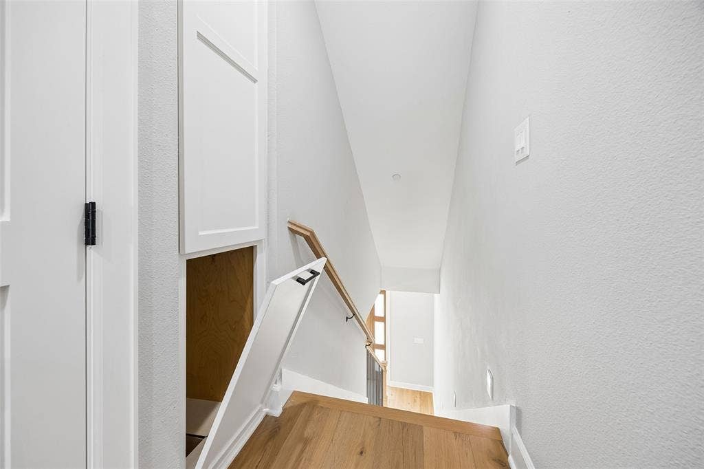 Staircase featuring wood-finish flooring, a wall-mounted wood handrail with matte black hardware, and built-in custom cabinetry with hidden storage access