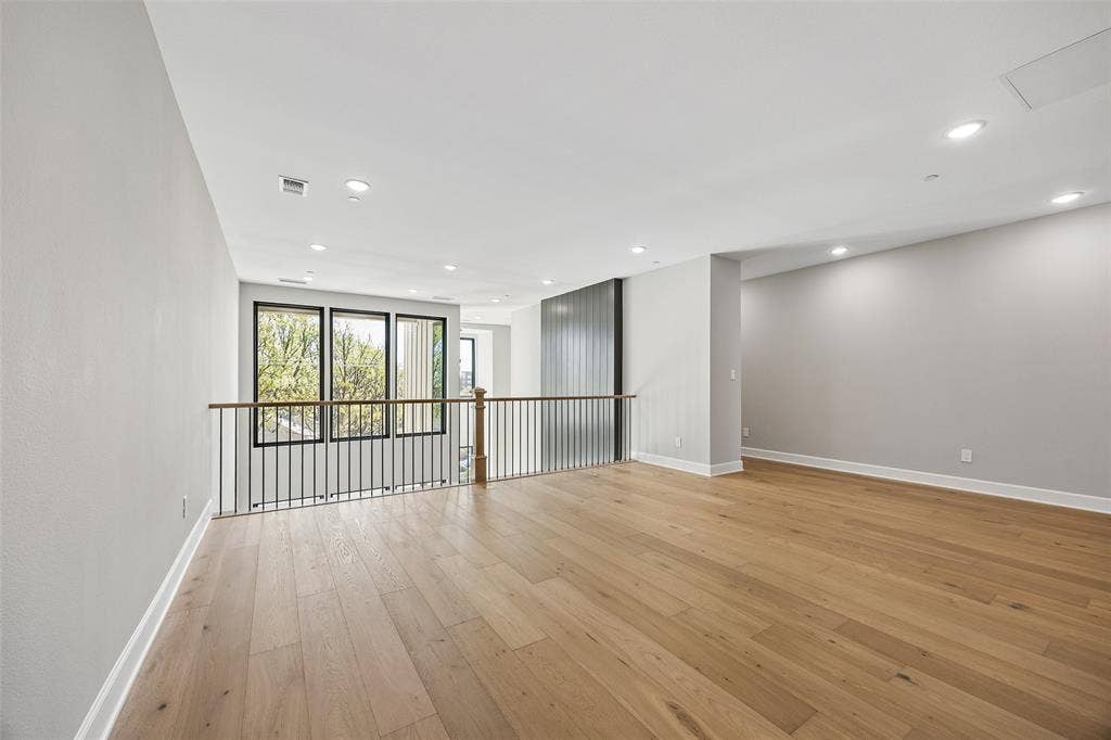 Open-concept interior featuring light-toned wood-finish flooring, recessed lighting, floor-to-ceiling windows with black frames, and a metal railing with a wooden handrail