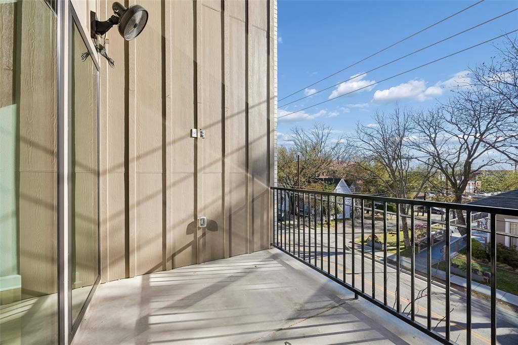Balcony featuring vertical board-and-batten siding, a black metal railing, and an attached exterior light fixture