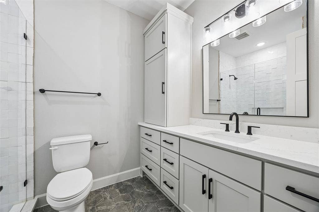 Bathroom featuring a light-toned vanity with integrated cabinetry, solid surface countertop, matte black fixtures, and hexagonal floor tiling