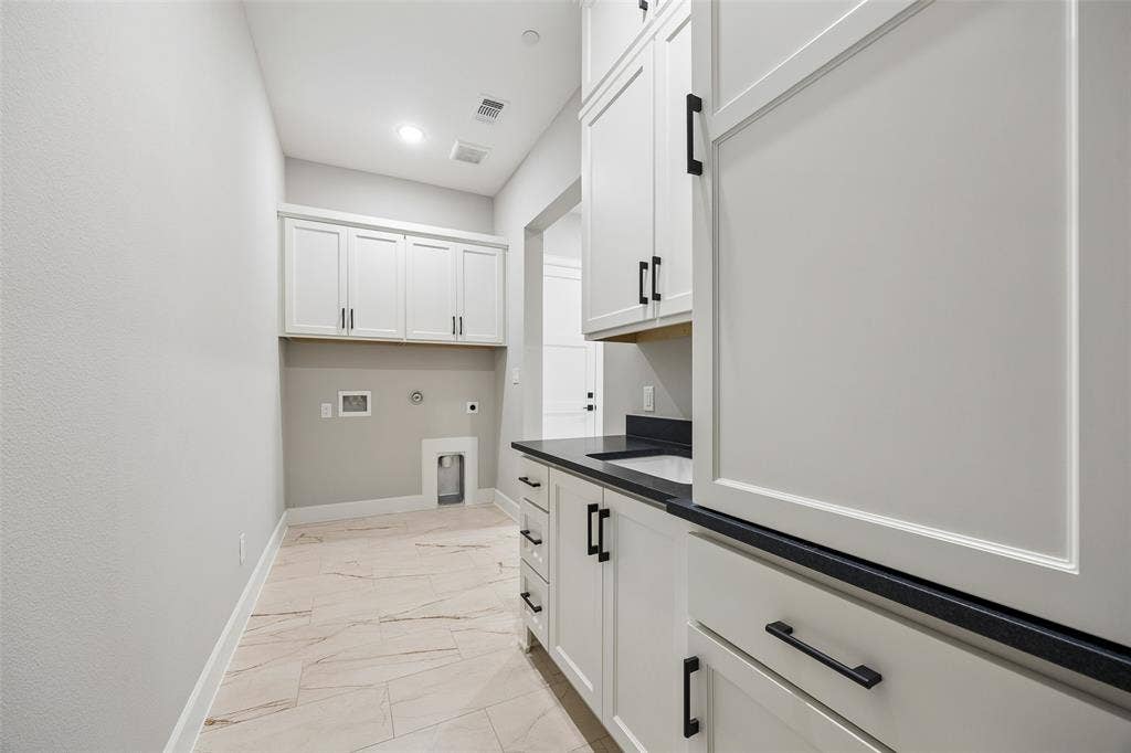 Laundry room featuring white cabinetry, dark countertops, integrated sink, and large-format tile flooring with matte black hardware