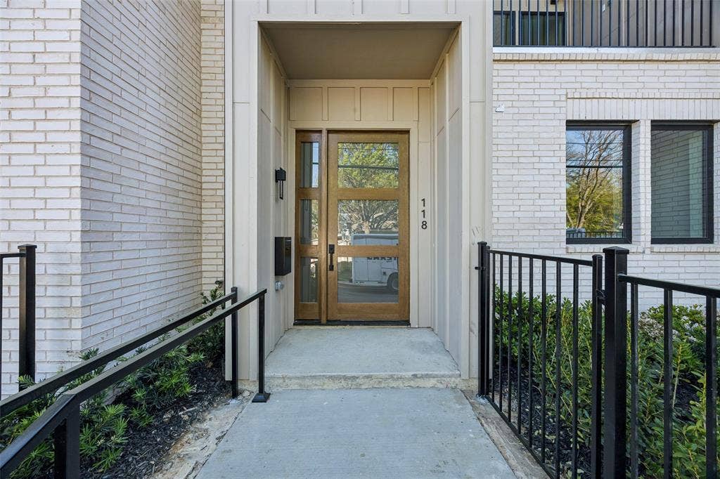 Off-white brick exterior featuring a wood-finish entry door with multi-lite glass panels, matte black metal railings, and framed windows with dark mullions