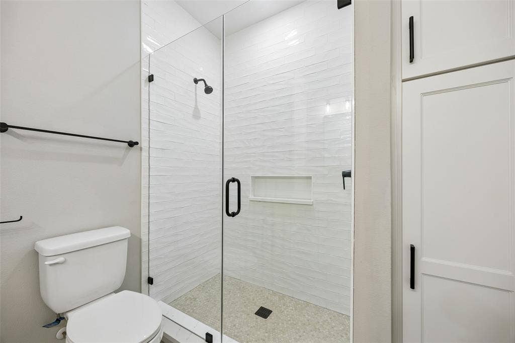 Walk-in shower featuring a frameless glass door, textured wall tile, integrated storage niche, and matte black hardware, accompanied by floor-to-ceiling built-in cabinetry