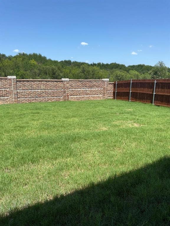 Backyard featuring a manicured lawn, brick perimeter wall with stone cap detail, and wood-slat fencing