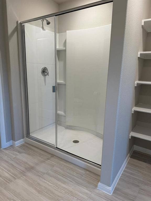 Shower enclosure with a curved glass sliding door, integrated shelving, a single-handle faucet fixture, and wood-finish tile flooring, accompanied by built-in wall shelving