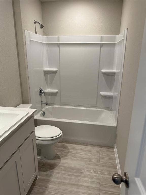 Bathroom featuring a white vanity cabinet with a integrated sink, wood-finish tile flooring, a porcelain toilet, and a white acrylic tub-shower combination with integrated shelving and chrome fixtures