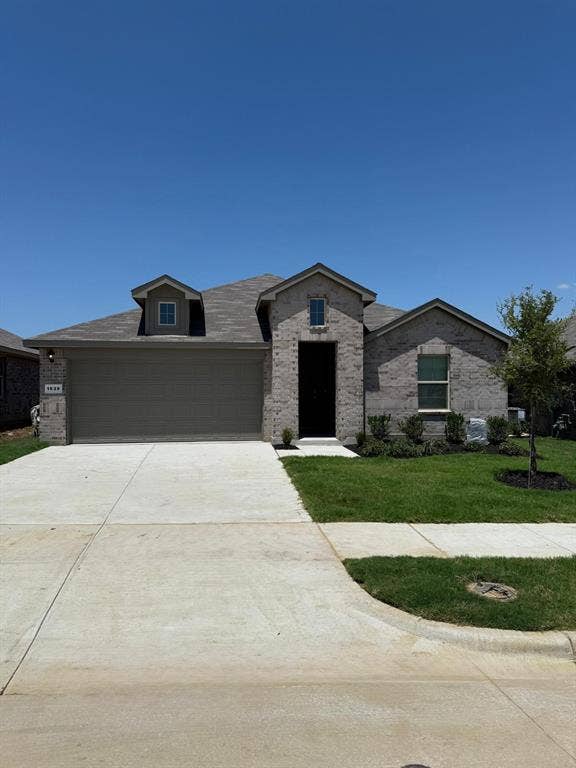 Brick exterior featuring a multi-gabled roofline, front-facing dormer, concrete driveway, and landscaped front yard