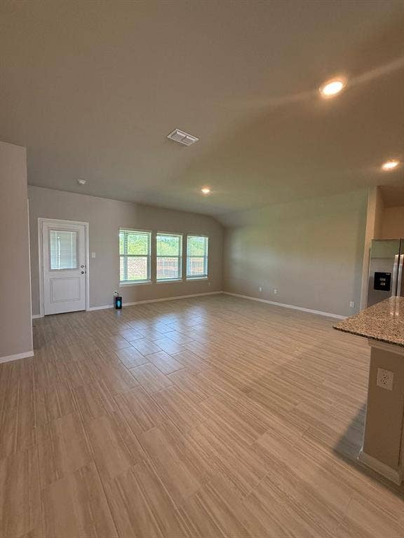 Open-concept area featuring wood-finish tile flooring, recessed lighting, neutral wall paint, and a trio of windows providing natural light