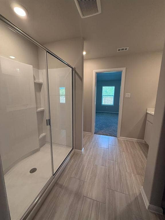 Walk-in shower with a glass enclosure, integrated shelving, and wood-finish tile flooring