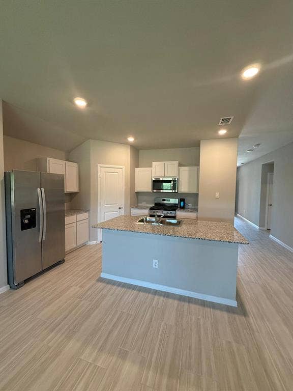 Kitchen featuring white cabinetry, stone-finish countertops, stainless steel appliances, a center island with a dual-basin sink, and wood-finish flooring