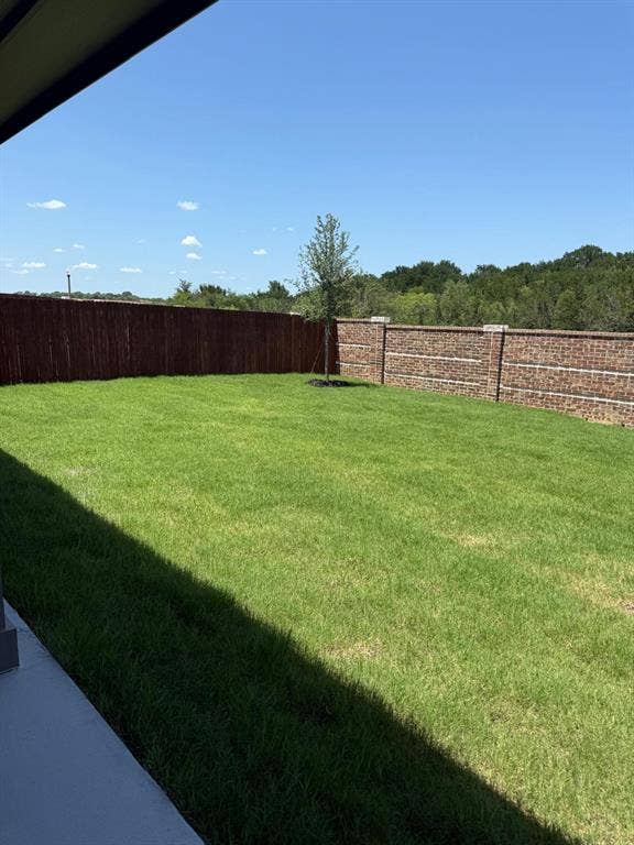 Backyard featuring a manicured lawn, masonry perimeter wall, wood-slat fencing, and mature trees