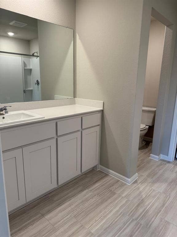 Bathroom featuring a vanity with white cabinetry, a solid-surface countertop with an integrated basin, a large wall-mounted mirror, and wood-finish flooring