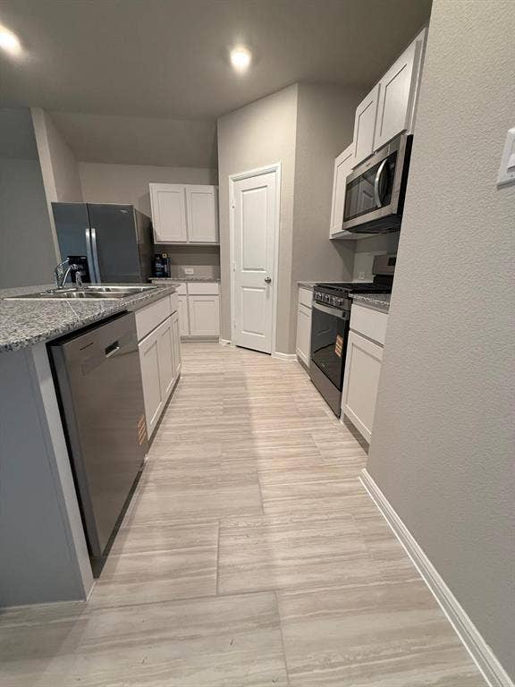 Kitchen featuring shaker-style white cabinetry, stone-finish countertops, stainless steel appliances, and large-format tile flooring