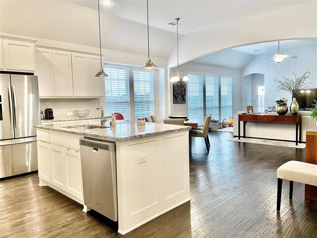 Kitchen featuring white shaker-style cabinetry, a stone-surfaced center island with an integrated stainless steel dishwasher, wood-finish flooring, and vaulted ceilings