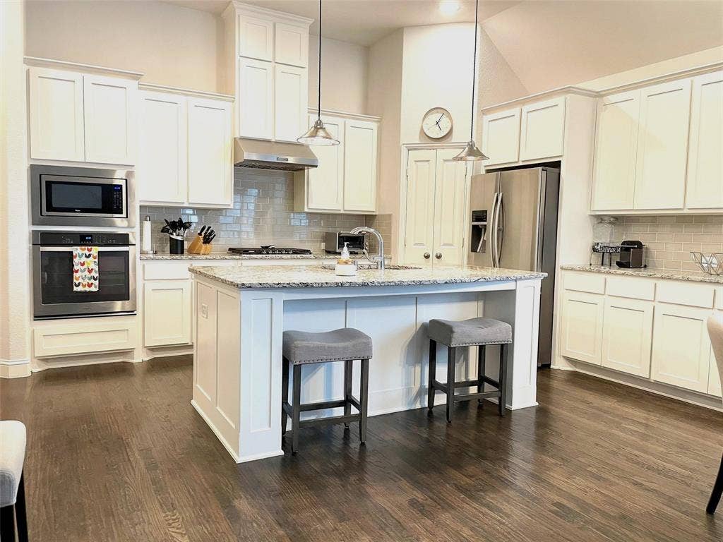 Kitchen featuring white cabinetry, stone-surface countertops, wood-finish flooring, stainless steel built-in appliances, and a central island with pendant lighting