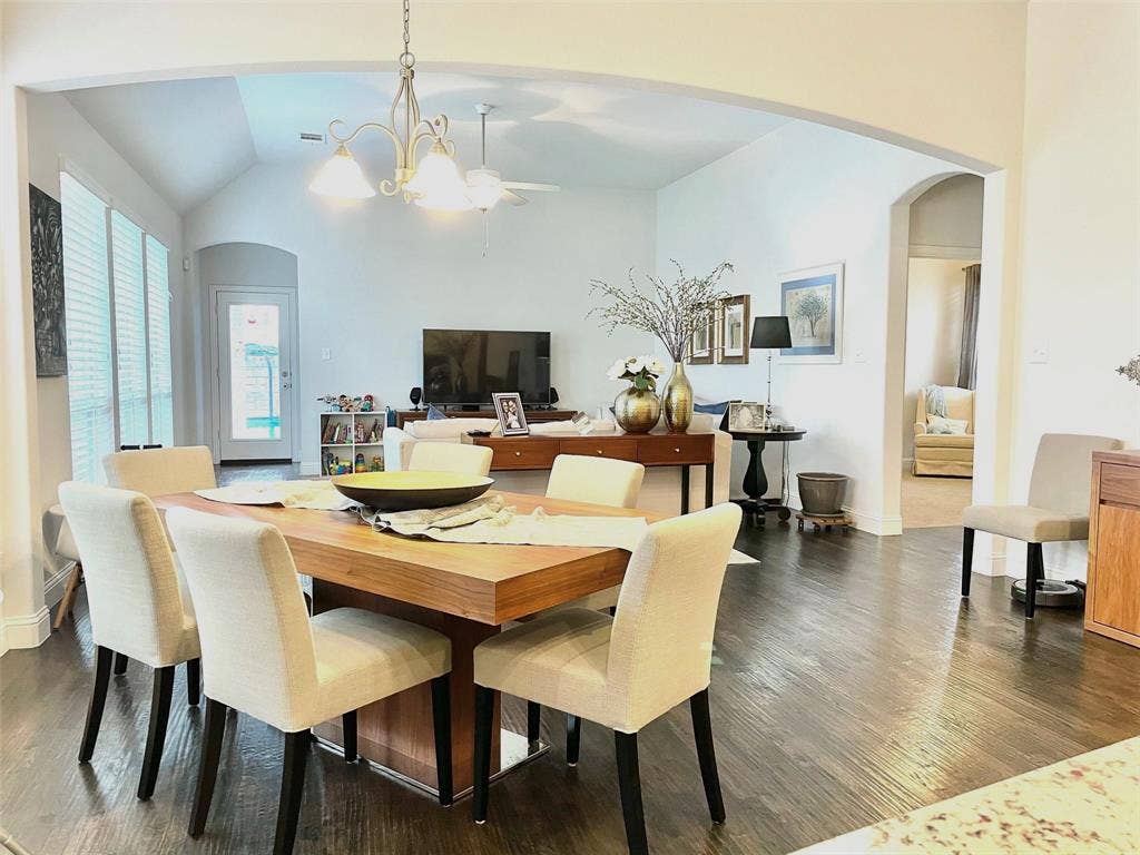 Open-concept interior featuring vaulted ceilings, dark wood-finish flooring, an arched entryway, and a tiered chandelier
