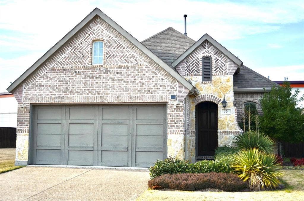 Traditional exterior featuring a brick and stone facade, herringbone masonry detailing, an arched entryway, and a multi-car garage